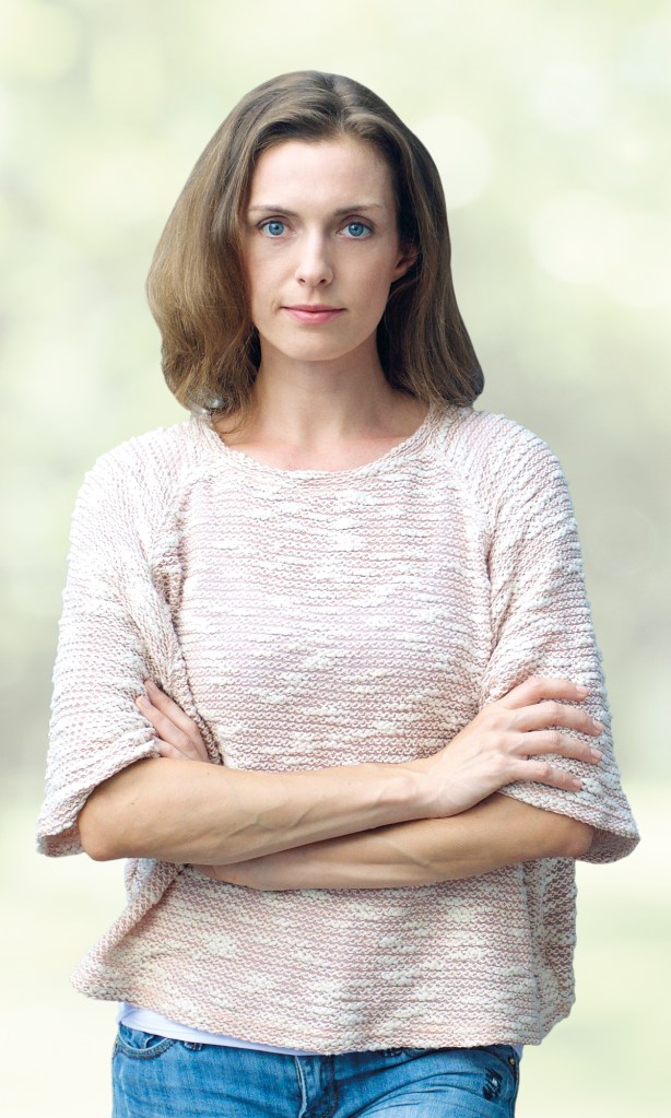 Anna standing in park with arms folded looking serious