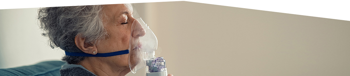 Elderly woman with eyes closed using a nebuliser