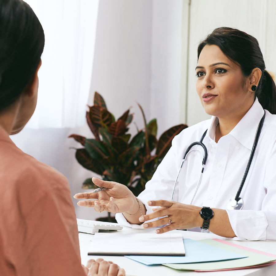Female doctor sat behind a desk talking to a patient.