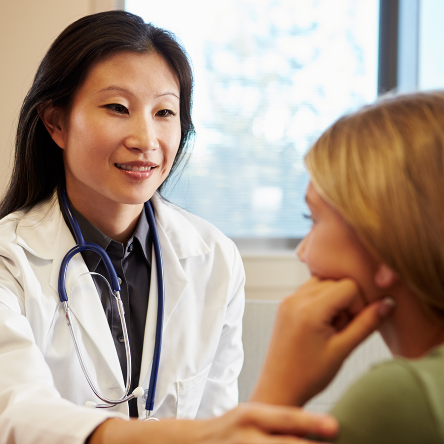 Female healthcare professional wearing a white coat in consultation with a young female patient.
